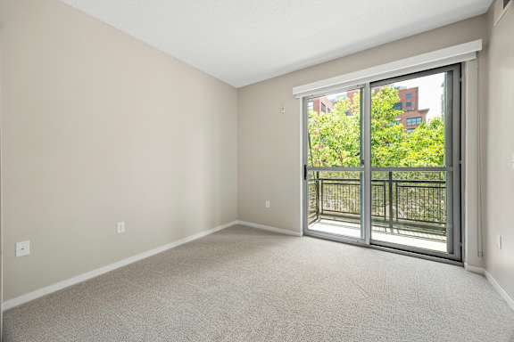 Empty room with a view of trees and a fence outside through the sliding glass door.