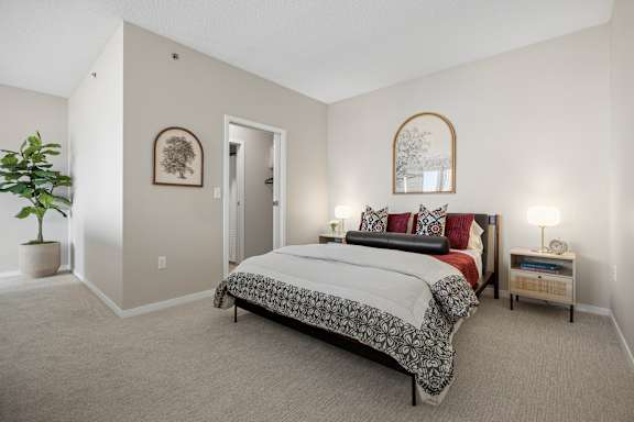 A bedroom with a large bed, a potted plant, and a mirror on the wall.