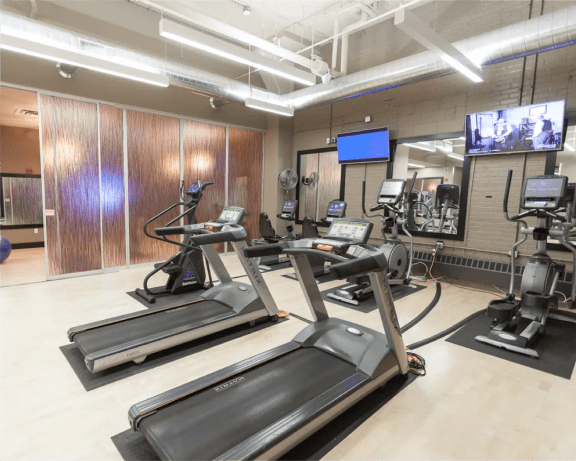 a gym with several treadmills and weights and a tv