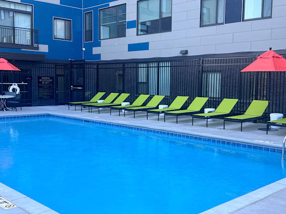 A pool with yellow and green sun loungers and a red umbrella.
