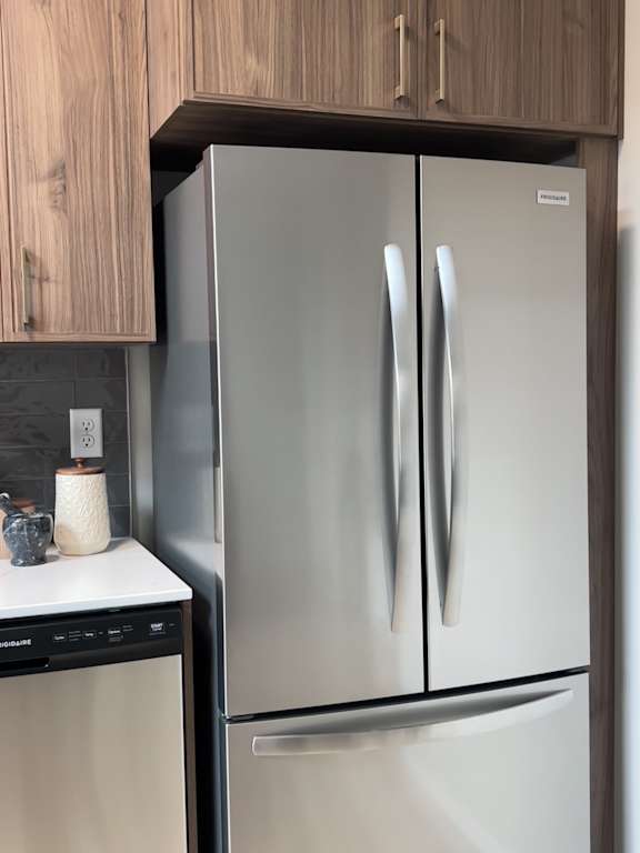 A stainless steel refrigerator with French doors next to a dishwasher in a kitchen.