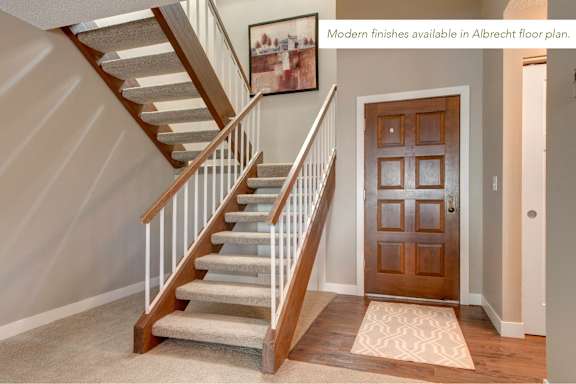 A staircase with a wooden handrail and beige carpeted steps leads to a door.