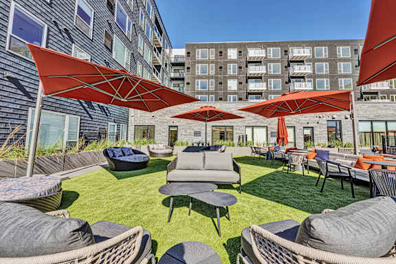 A large outdoor seating area with red umbrellas and grey couches. at The Mera, Minnesota, 55426