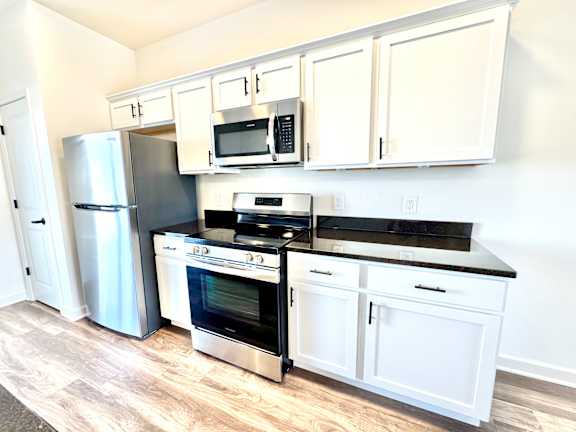 A kitchen with white cabinets and black countertops.at Concord Crossing, Indiana