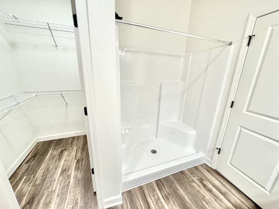 A white walk-in shower with a glass door is in a room with wood flooring.at Concord Crossing, Lafayette Indiana