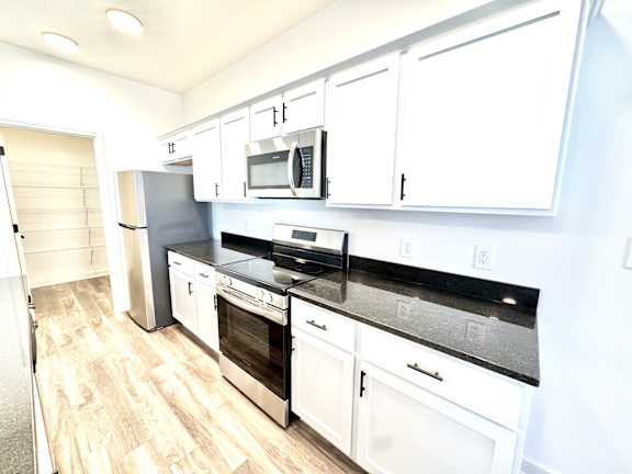 A kitchen with white cabinets and black countertops.at Concord Crossing, Indiana