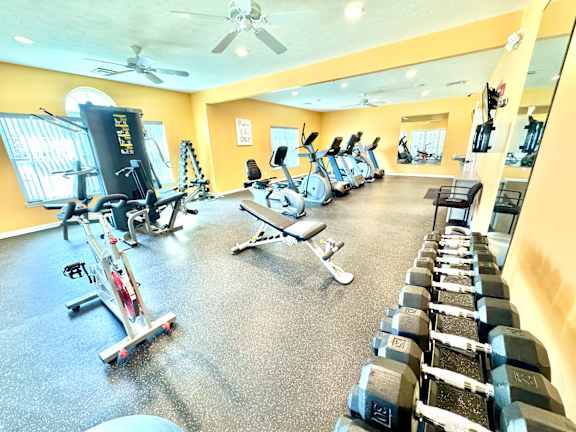 A gym with a variety of equipment including treadmills, stationary bikes, and dumbbells.