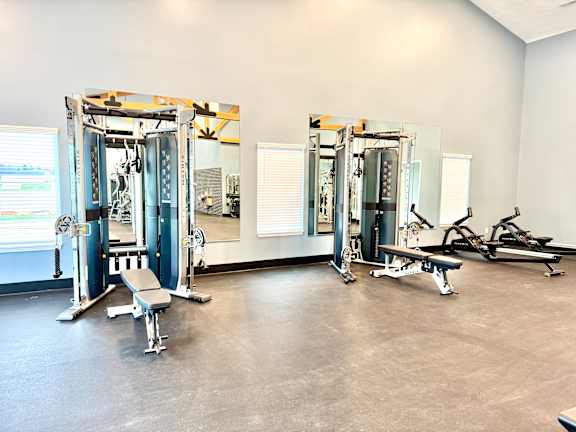 A gym with a row of squat racks and a bench.at Concord Crossing, Lafayette Indiana