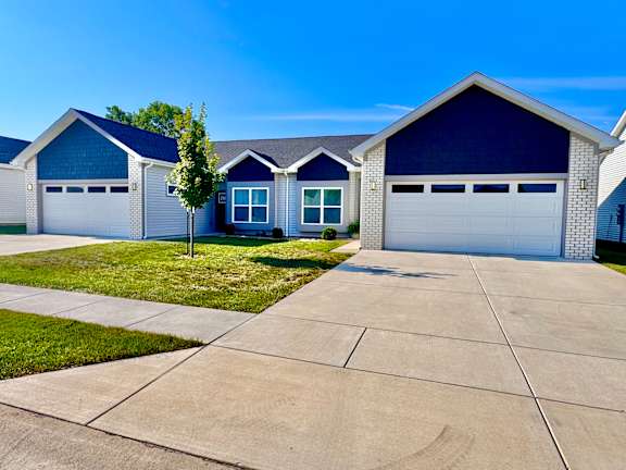 A blue house with a white garage door is in front of a green tree.