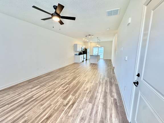 A long hallway with wood flooring and a ceiling fan.