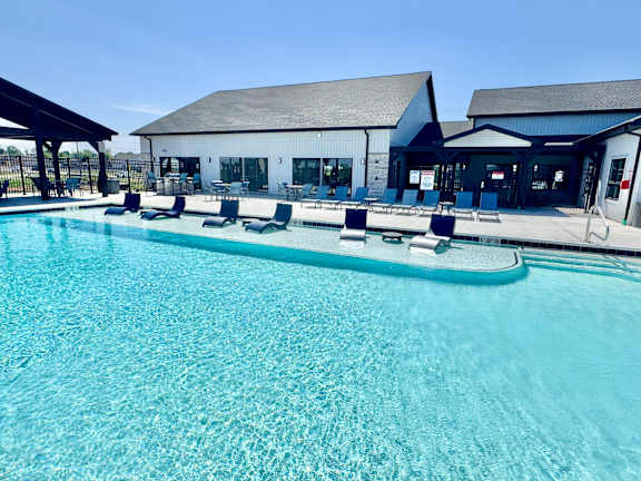 A large swimming pool with lounge chairs and a building in the background.