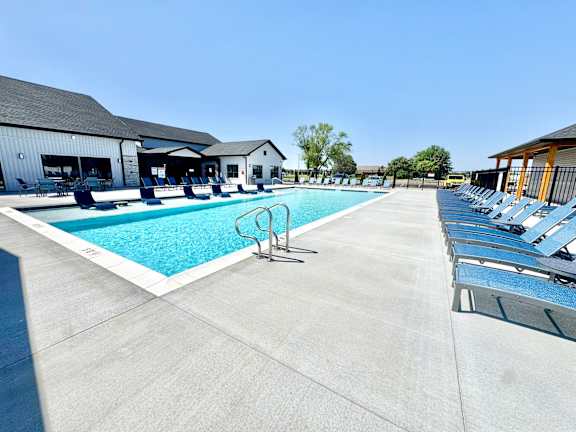 A large swimming pool with lounge chairs and a building in the background.