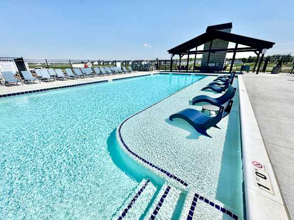 A large swimming pool with blue seats and a pavilion.
