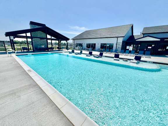 A large outdoor swimming pool with a concrete edge and a white concrete pool deck.