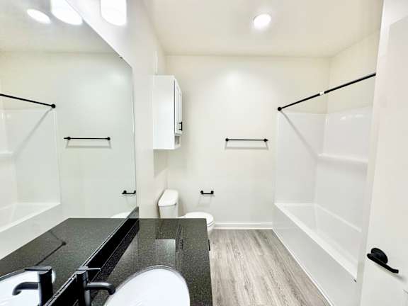 A white bathroom with a black counter top and a white toilet.