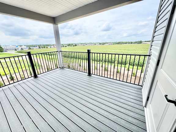 A wooden deck with a black railing overlooks a green field.