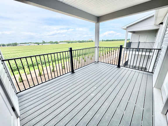 A wooden deck with a metal railing overlooks a green field.