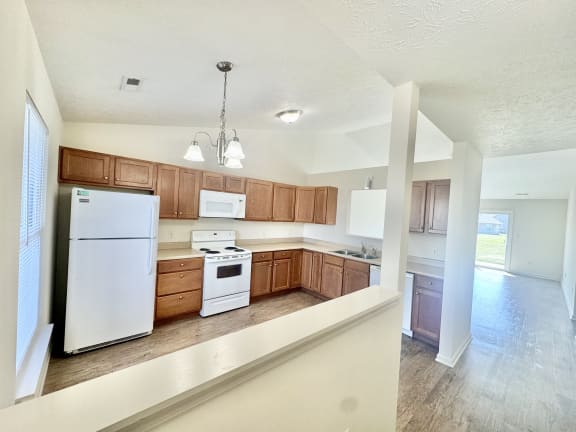 an empty kitchen with white appliances and wooden cabinets at Hawthorne Properties in Lafayette, IN 47905