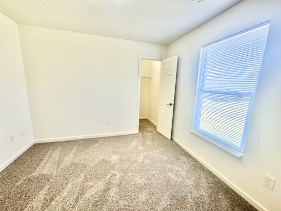 an empty bedroom with a large window and carpeted flooring at Hawthorne Properties in Lafayette, IN 47905