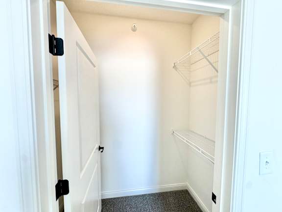 A white closet with a door open and a shelf on the wall.