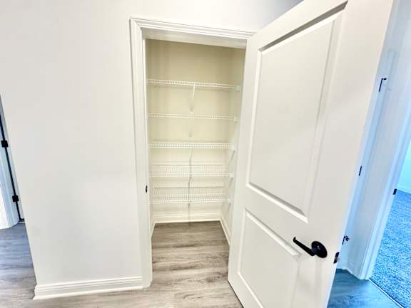 A white door with a black handle is open to a room with a white wall and a grey floor.