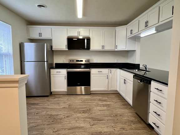 A kitchen with white cabinets and black countertops.