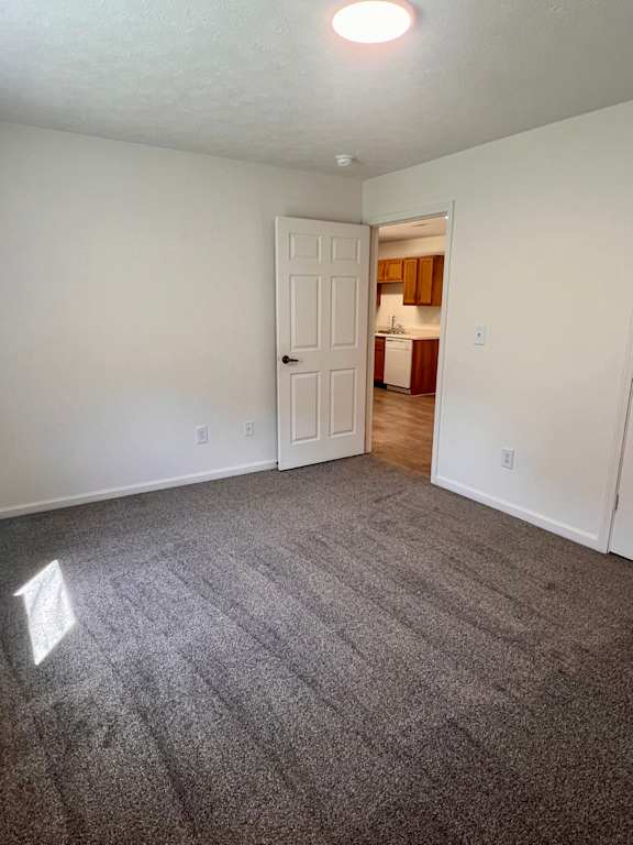 A room with a carpeted floor and a door leading to a kitchen.