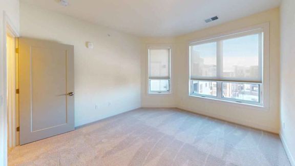 A room with a door, two windows and a carpeted floor.