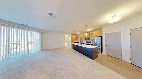 A spacious living room with a kitchen area in the background.