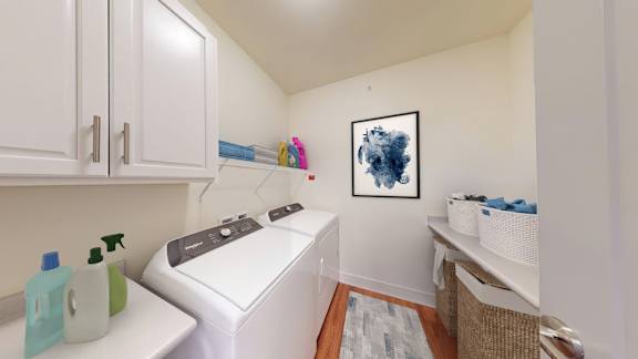 A laundry room with a washer and dryer, a basket, and a picture on the wall.
