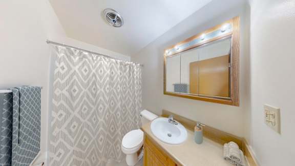 A bathroom with a white sink, mirror, and shower curtain.