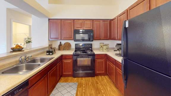 A kitchen with a black refrigerator, wooden cabinets, and a black stove top oven.
