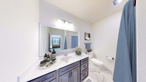 A bathroom with a sink, mirror, toilet, and a blue shower curtain.
