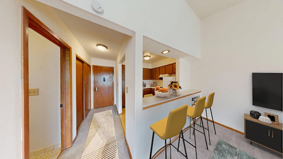 A hallway with a striped carpet leads to a kitchen area with a bar and chairs.