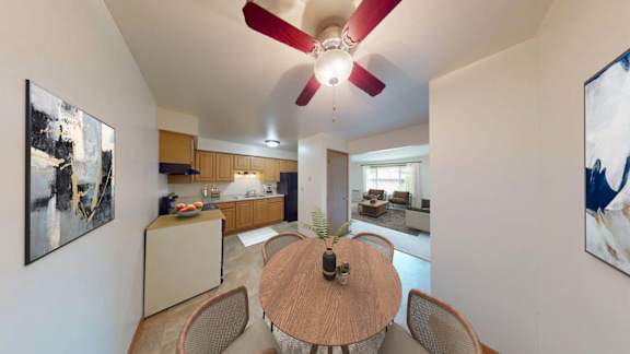 A living room with a ceiling fan and a dining table with chairs.
