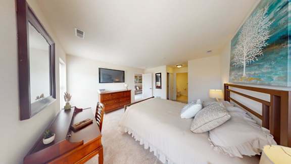 A bedroom with a large bed, a desk, and a painting on the wall.