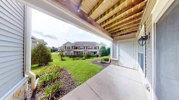 A view from a covered walkway looking out to a grassy area with houses in the distance.