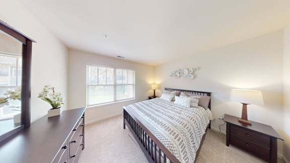 A bedroom with a large bed, a nightstand with a lamp, and a window with a view of the city.