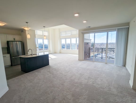 an empty living room with a kitchen and a balcony