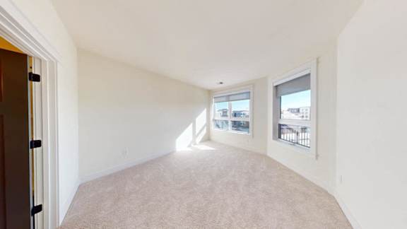 A room with white walls and carpeted floor with two windows.