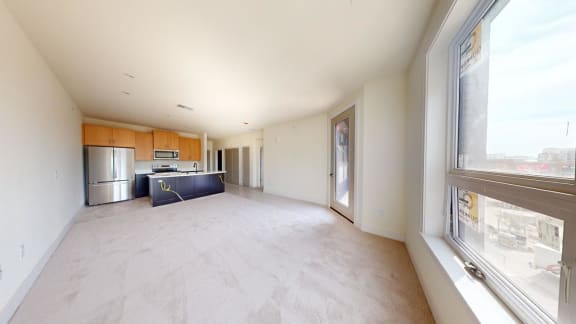 an empty living room with a kitchen and a large window