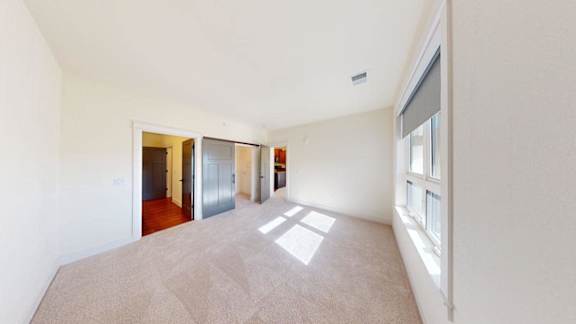 A spacious room with a carpeted floor and a large window on the right side.