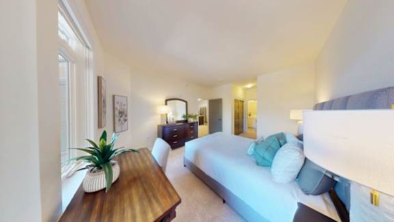 A bedroom with a bed, a dresser, and a plant on a wooden table.