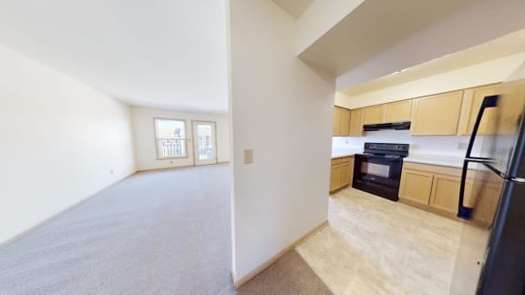 a large empty living room and kitchen with black appliances