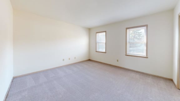 a spacious living room with carpeting and two windows