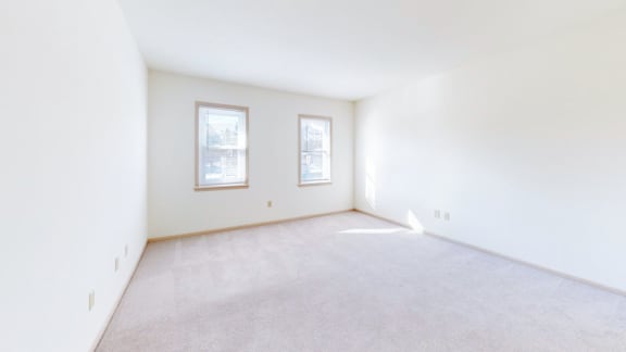 a living room with white walls and carpet and two windows