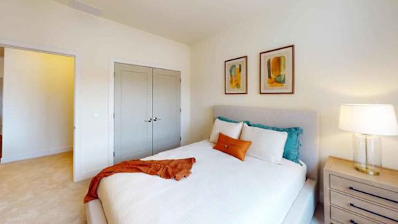 A bedroom with a white bed, a red blanket, and two framed pictures on the wall.