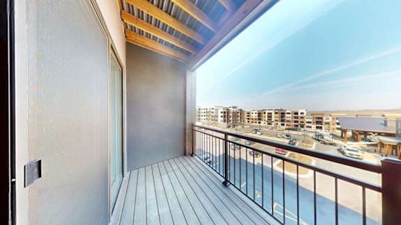 A balcony with a view of a parking lot and buildings.