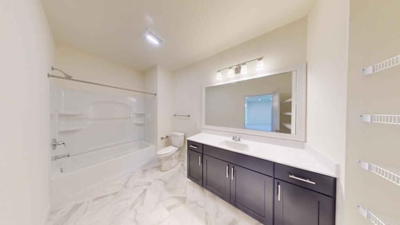 A white bathroom with a marble floor and black cabinets.