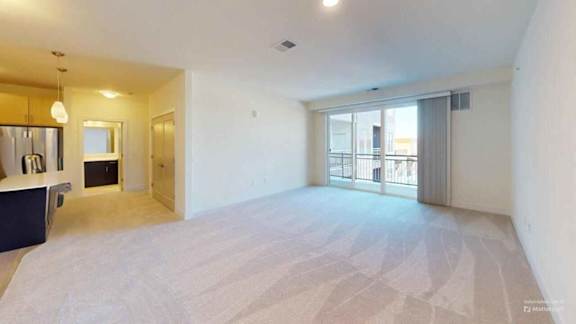A spacious, empty room with a bar area and a sliding glass door leading to a balcony.